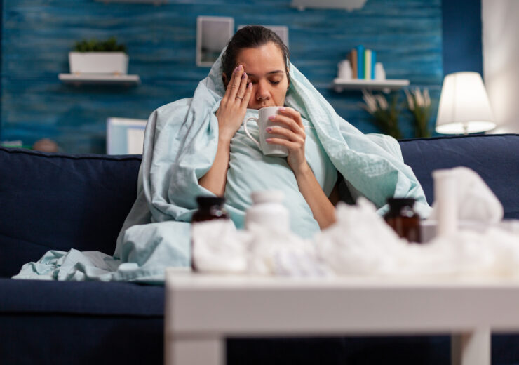 Sick woman sitting at home in blanket with hot tea